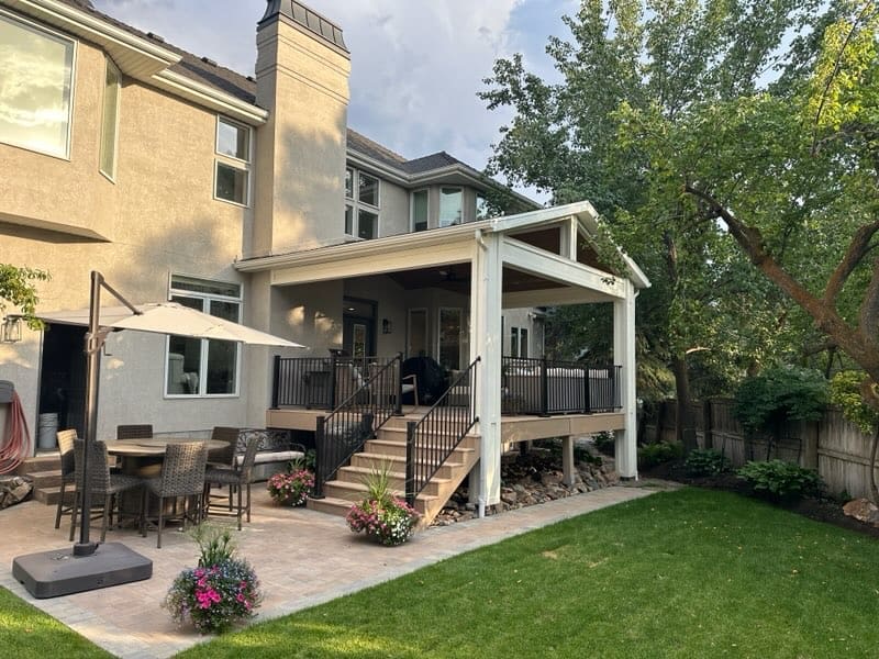 Covered deck with a white gabled patio cover, paver patio and dining set behind a Utah home