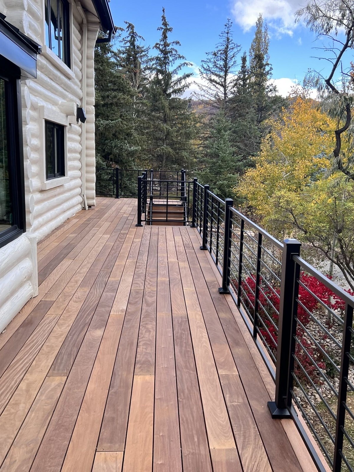 Ipe hardwood deck walkway with black horizontal-rod railing beside a log home