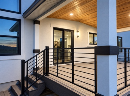 Covered composite deck with black horizontal-rod railing and stairs at twilight