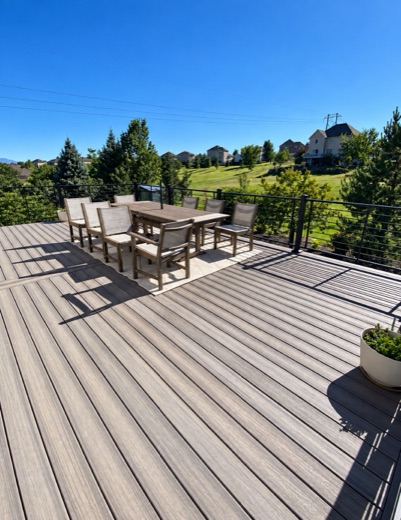 Wide gray composite deck with a dining set and black cable railing above a golf course