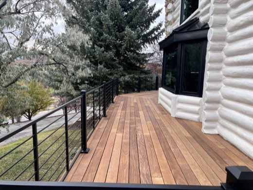 Ipe hardwood deck along a log home bay window with black horizontal-rod railing