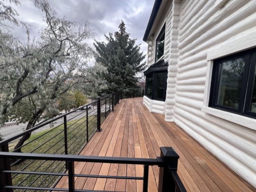 Ipe hardwood walkway deck wrapping a white log home with black horizontal-rod railing