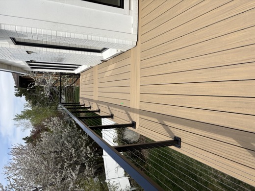 Raised tan composite deck beside white brick house with black cable railing (TimberTech)