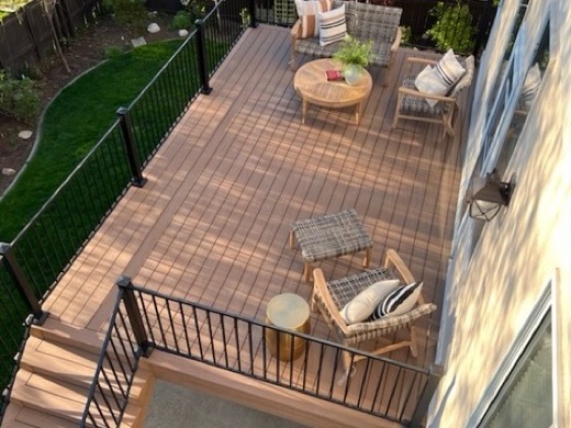 Raised brown composite deck with black metal railing, stairs and patio seating beside lawn