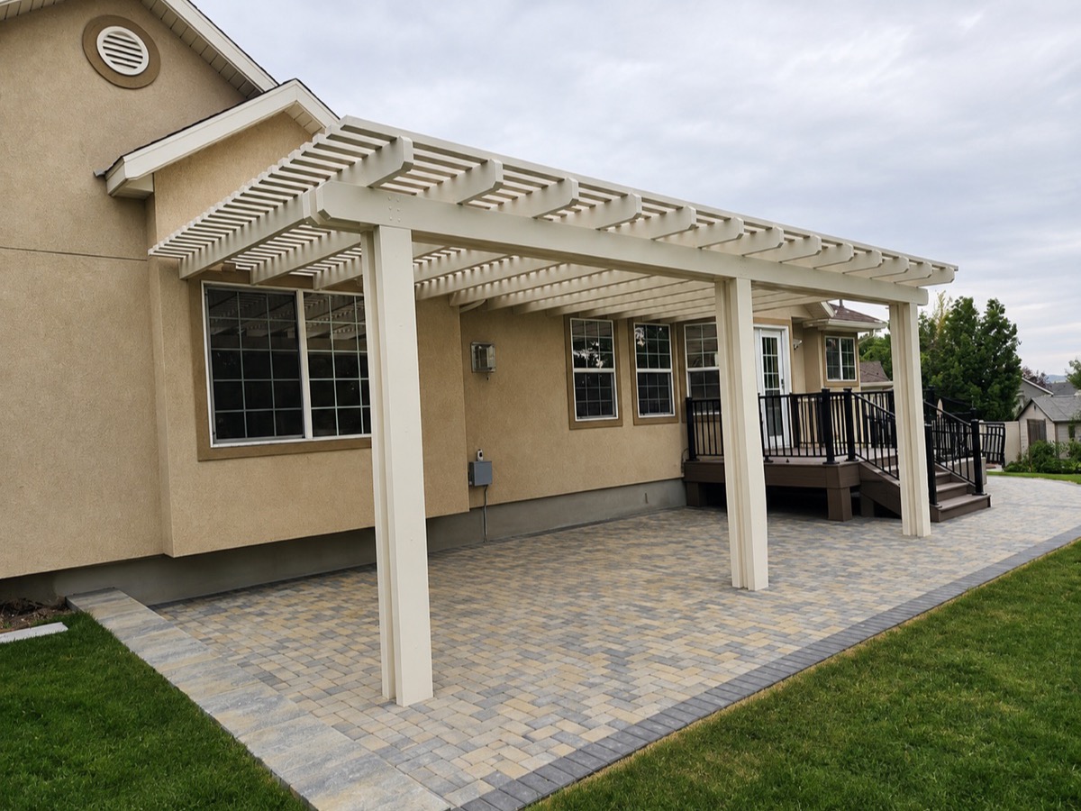 Cream attached pergola over a paver patio beside a stucco home