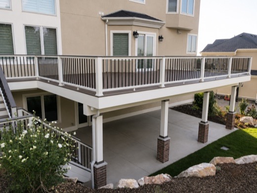 Elevated composite deck on white posts above a concrete patio
