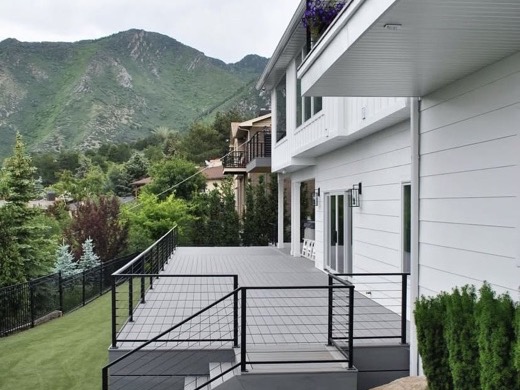 Grey composite deck with cable railing stepping down beside a home in the foothills