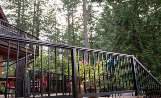 Black metal picket railing along deck and stairs surrounded by tall evergreen trees