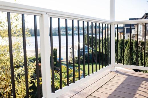 White railing with black metal balusters on covered deck overlooking water and trees