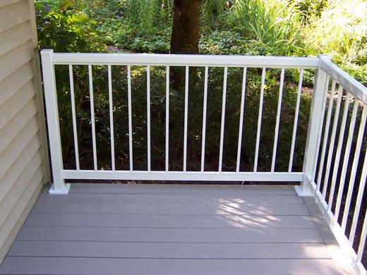 White vertical picket railing on gray composite deck facing shaded green backyard