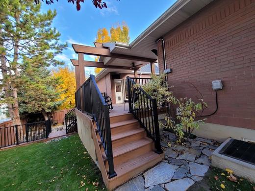 Brown composite deck with black metal picket railing, stairs and pergola beside brick home (Trex Signature)