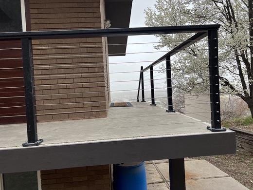 Black cable railing with square posts along concrete deck beside brick house (Precision railing)