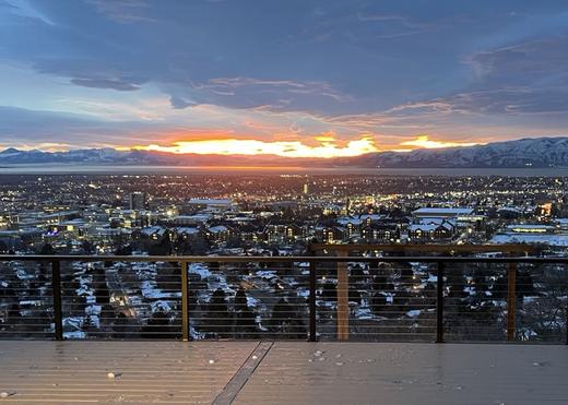 Cable railing with wood-look top rail framing city and mountain sunset view (Precision railing)