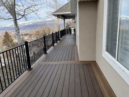 Brown composite deck with black metal picket railing overlooking snowy mountain valley (Cinch railing)