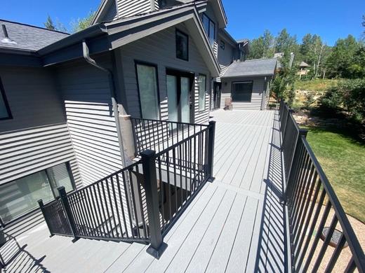 Gray composite deck with black metal picket railing and stairs beside hillside home (Cinch railing)