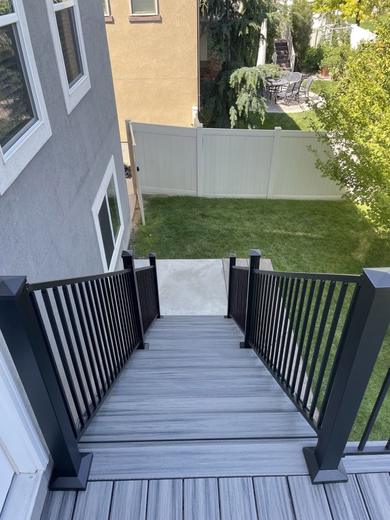 Black metal picket railing along gray composite deck stairs down to backyard lawn (Cinch railing)