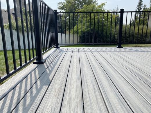 Black aluminum picket railing around gray composite deck boards with green backyard (Cinch railing)