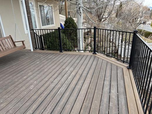 Black metal picket railing around a brown composite deck with porch swing (Cinch railing)