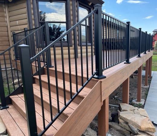Black metal picket railing along brown composite deck and stairs at log home (Cinch railing)
