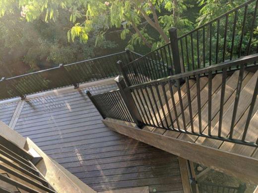 Black metal picket railing along curved deck stairs with brown wood decking and trees (Cinch railing)