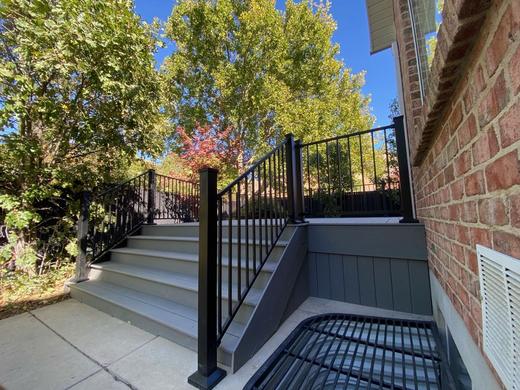 Black metal picket railing along gray composite steps beside brick house wall (Cinch railing)