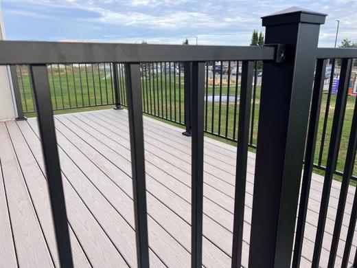 Black aluminum picket railing with post cap on gray composite deck overlooking open lawn (Cinch railing)