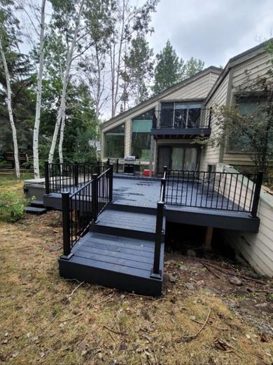 Gray deck with black metal picket railing and wide stairs beside wooded home (Cinch railing)