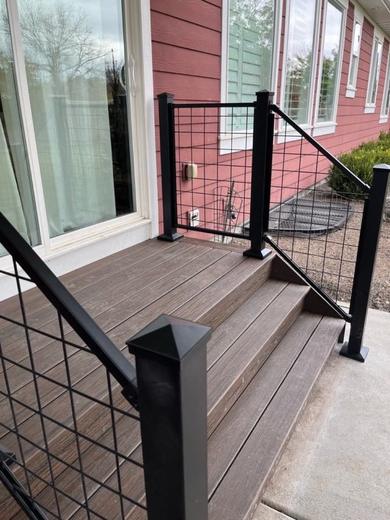 Small composite deck with black wire mesh railing and steps beside red siding (Cinch railing)