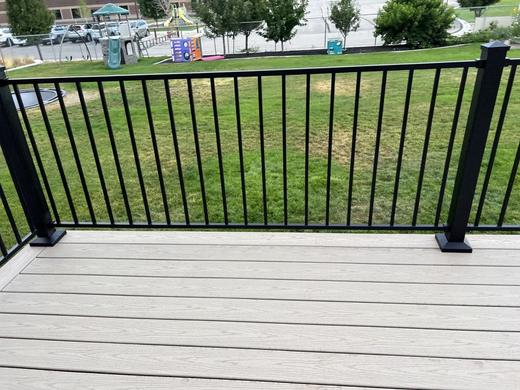 Black metal picket railing on light gray composite deck overlooking grassy lawn and park (Cinch railing)