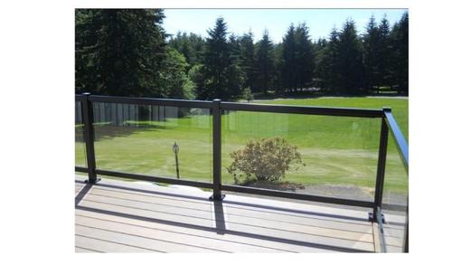 Glass panel railing with black frame on light deck overlooking green lawn and trees