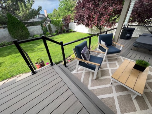 Black cable railing around a gray composite deck with a glass panel corner
