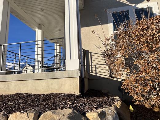 Black horizontal rod railing on covered porch with stucco walls and mulch beds