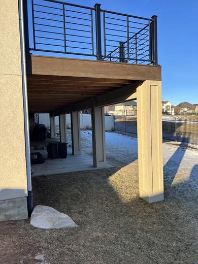 Elevated deck with black horizontal rod railing, brown fascia, stucco columns below, distant hills