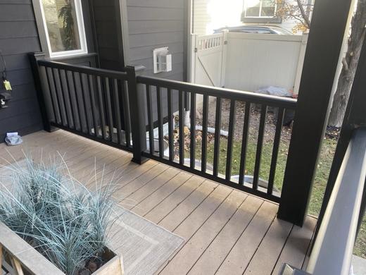 Black metal picket railing along tan composite deck beside white fence and house
