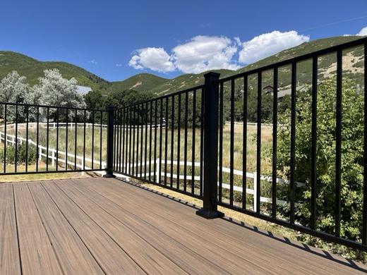 Black metal picket railing on brown composite deck with green mountain views