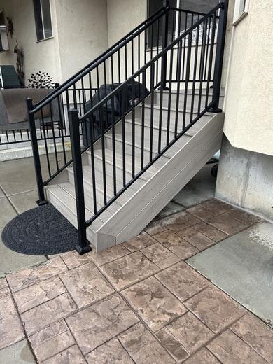 Black metal picket railing along gray composite steps beside stamped concrete patio