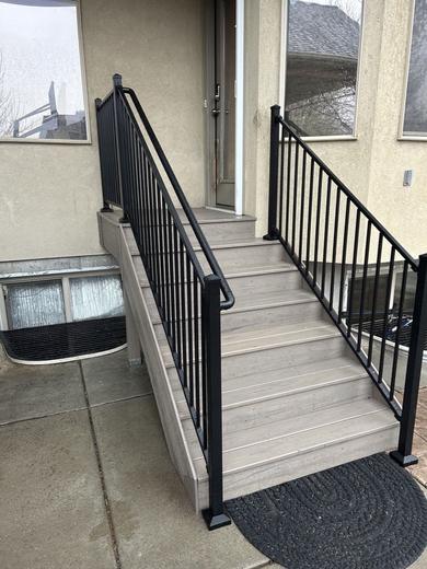 Black metal picket railing along gray composite entry steps at a stucco home