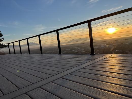 Cable railing with black posts on gray composite deck overlooking valley at sunset (Precision railing)