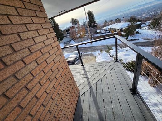 Black cable railing on gray deck beside brick wall overlooking snowy valley (Precision railing)