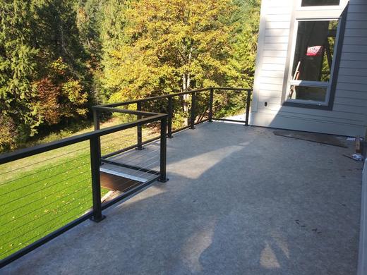 Black cable railing along concrete deck with stair opening and forest view (Precision railing)