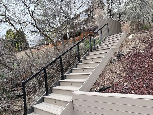 Black cable railing along tan composite stairs climbing a rocky landscaped hillside (Precision railing)
