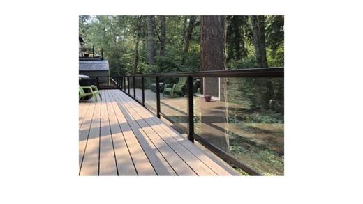 Glass panel railing with dark metal posts on a wood deck among trees (Precision railing)