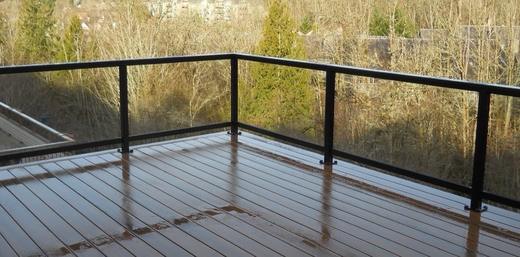 Wet brown deck with black posts and horizontal cable railing overlooking bare trees (Precision railing)