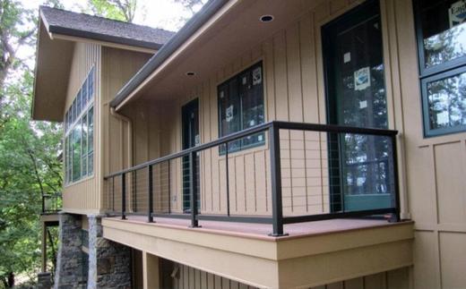 Black cable railing on raised deck with tan siding and wooded surroundings (Precision railing)