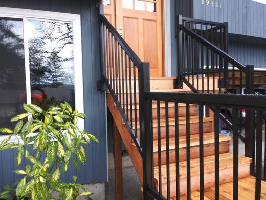 Black metal picket railing along wood entry stairs beside blue siding and door (Precision railing)