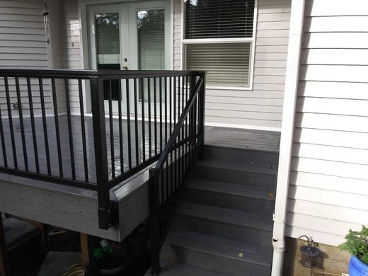 Black metal picket railing along gray deck with stairs beside light siding (Precision railing)