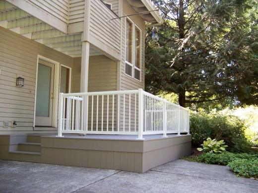 White vertical picket railing around low front porch deck with steps beside house (Precision railing)