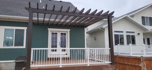 White picket railing on backyard deck under dark brown pergola beside green siding (Precision railing)