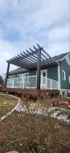 White picket railing on raised deck with brown pergola beside green siding home (Precision railing)