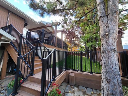 Raised backyard deck with black metal picket railing, wood stairs and brown decking (Trex Select)